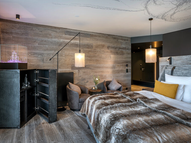 Modernes Doppelbett mit Felloptik-Überwurfdecke, daneben zwei Sessel, Stehlampe und Beistelltisch