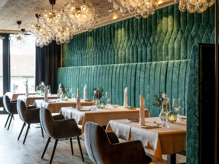 Modernes Restaurant mit Kronleuchtern und grüner Samtbank im 4-Sterne-Hotel Hüttenhof