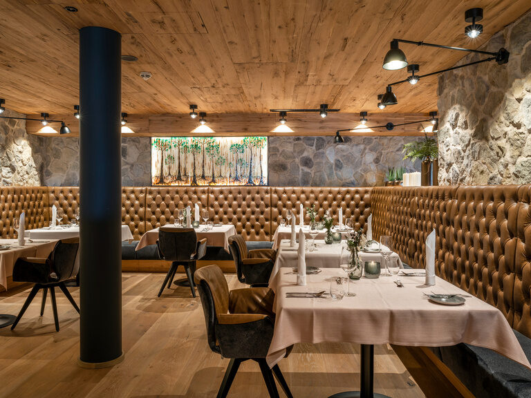 Modernes Restaurant mit eingedeckten Tischen, brauner Leder-Sitzbank und Steinwand