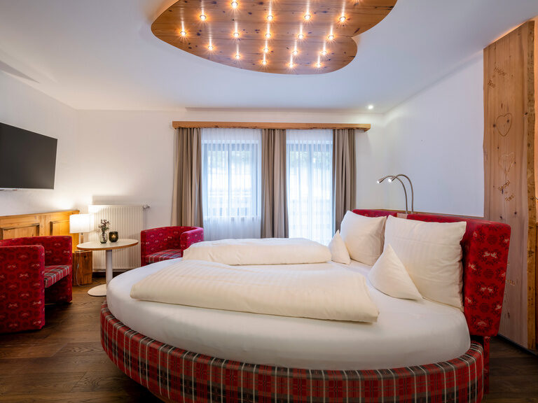Modernes Romantik-Zimmer mit rundem Bett im Wellnesshotel Hüttenhof Romantisches Zimmer mit rundem Bett und herzförmiger Holzplatte mit Glühbirnen