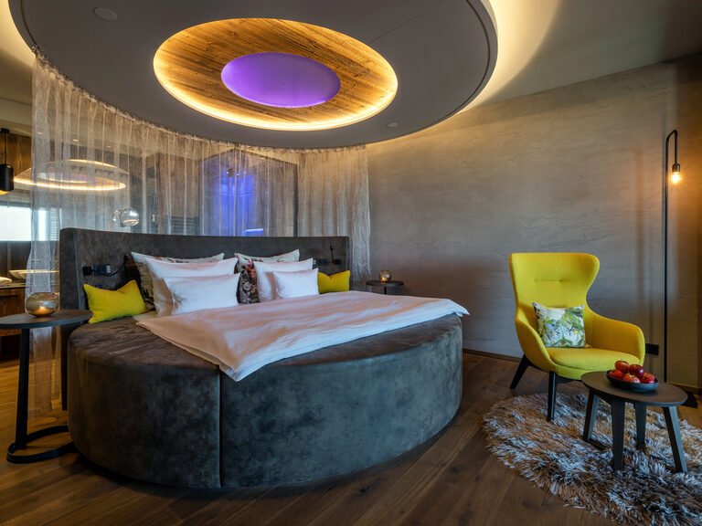 Modernes rundes Bett, daneben sessel mit beistelltisch, darüber große Wandleuchte