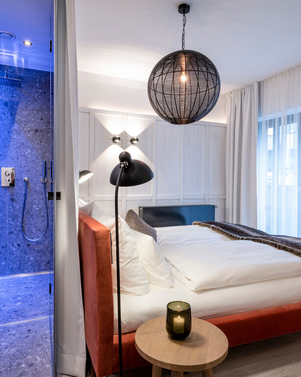 Modernes Zimmer in minimalistischer Einrichtung mit beleuchteter Dusche, Doppelbett und Balkon