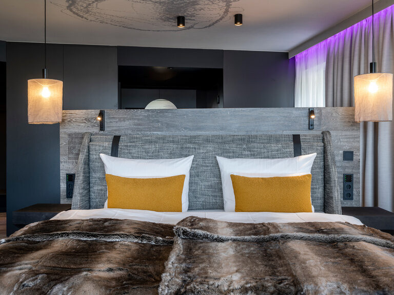 Nahaufnahme Vorderansicht von modernem Doppelbett mit zwei Hängelampen und Überwurfdecken in Felloptik