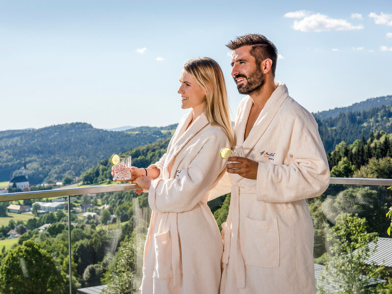 Paar in Bademäntel auf Balkon mit Drinks genießt Ausblick aus 4-Sterne-Hotel Hüttenhof