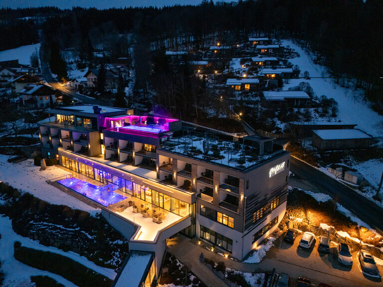 Paar im 4-Sterne-Luxushotel Hüttenhof stößt lachend mit Sektgläsern an. Glückliches Paar stößt in der Lounge mit Sektgläsern an, während sie sich liebevoll anblicken