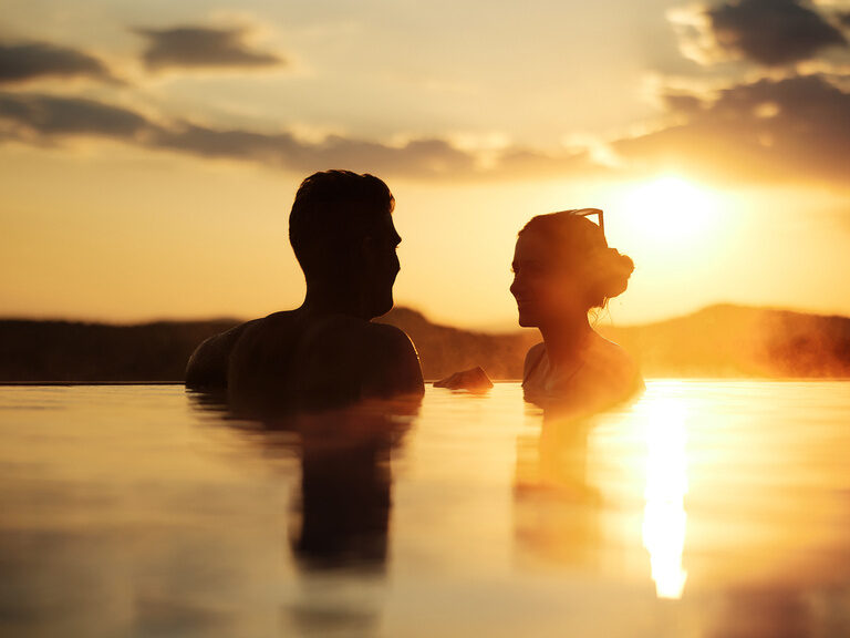 Paar in Außenpool vom Wellnesshotel Hüttenhof bei Dämmerung Schattenansicht von Paar im Außenpool vom Wellnesshotel Hüttenhof bei Dämmerung