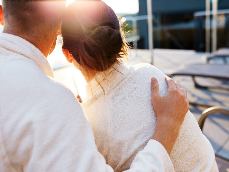 Paar in Bademantel genießt Sonne auf der Terrasse vom Luxushotel Hüttenhof Rückenansicht von Paar im Bademantel, das Sonne auf Terrasse vom Hotel genießt
