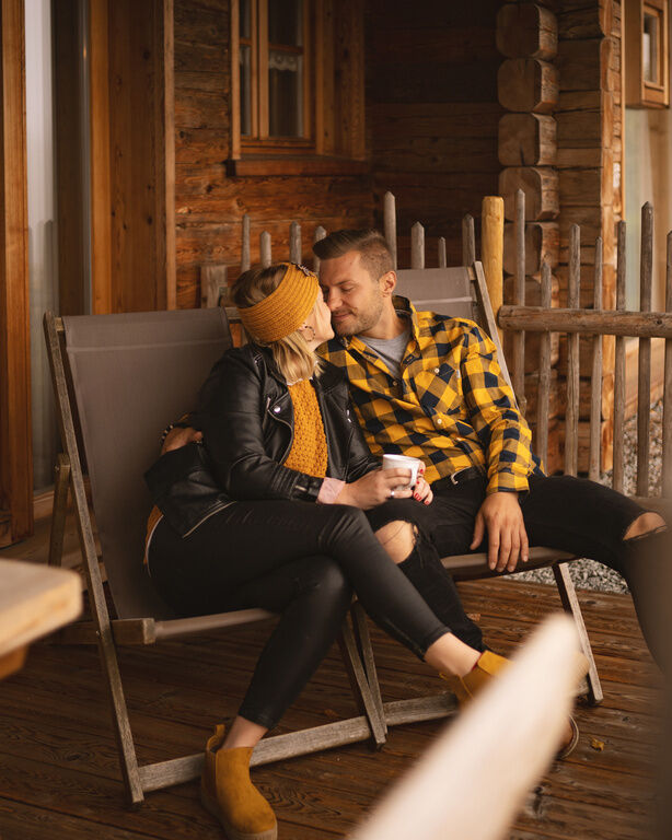 Liebespaar sitzt auf auf der Terrasse einer idyllischen Holzhütte bei einem Kuss