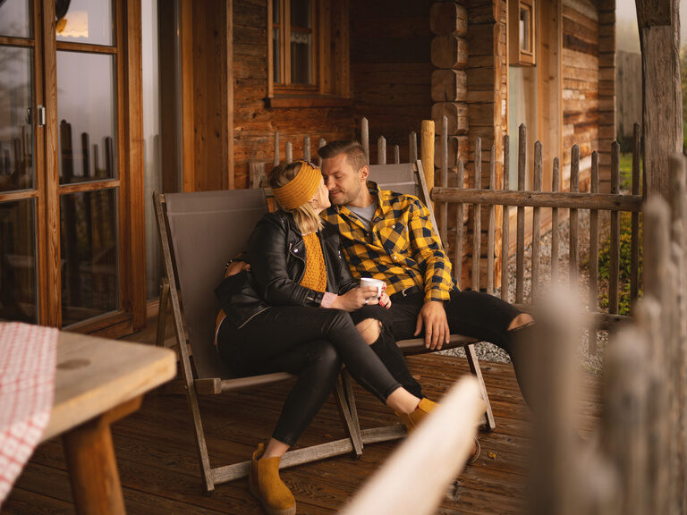 Liebespaar sitzt auf auf der Terrasse von idyllischen Holzhütte bei einem Kuss