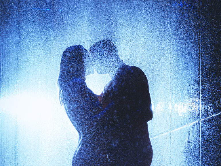 Schattenansicht von Paar, das sich unter Wasserfall-Dusche küsst
