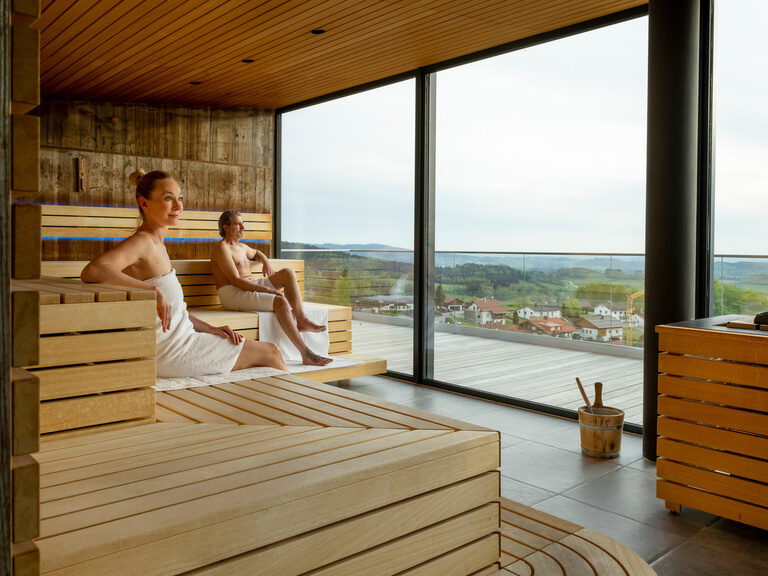 Paar sitzt in moderner Panoramasauna vom Luxushotel Hüttenhof Paar sitzt in moderner Panoramasauna vom Wellnesshotel-Hotel Hüttenhof