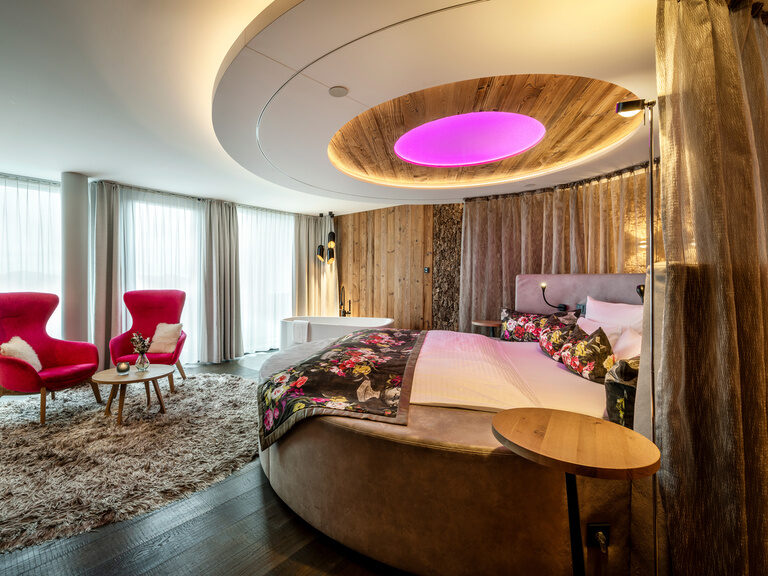 Paar liegt mit Rücken auf dem Bett, stößt mit Sektgläsern an und zeigt Peace-Handzeichen