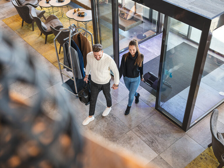 Verliebtes Pärchen geht Hand in Hand mit Gepäck zum Check In des 4 Sterne Luxushotel Hüttenhof in Niederbayern Pärchen geht Hand in Hand mit Gepäck zum Check In des 4 Sterne Wellnesshotel Hüttenhof im Bayerischen Wald