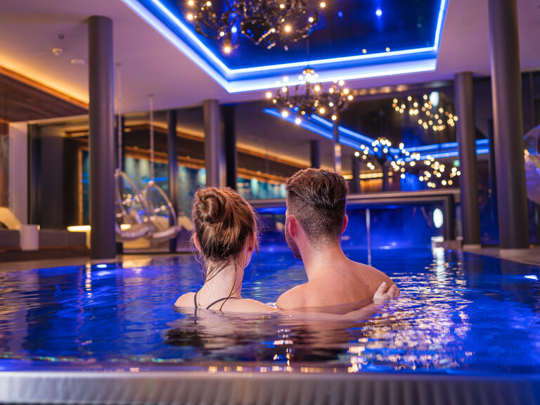 Pärchen schwelgt Arm in Arm am Abend im Hallenbad des 4 Sterne Wellnesshotel Hüttenhof im Bayerischen Wald
