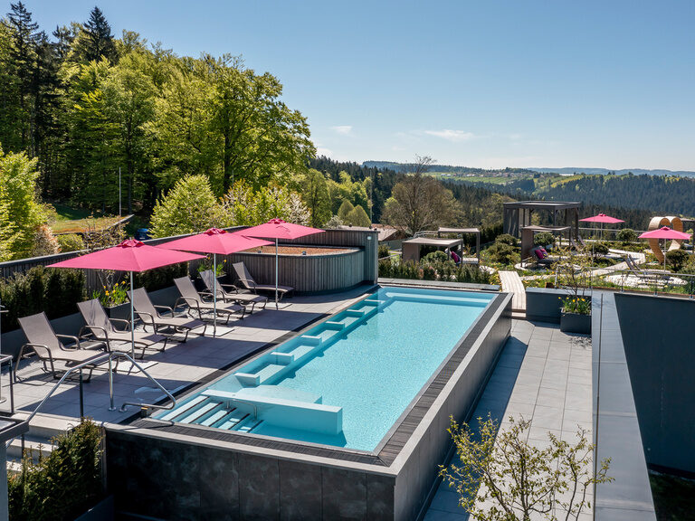 Pool auf sonniger Dachterrasse mit Sonnenschirmen und Waldpanorama vom Hotel Hüttenhof
