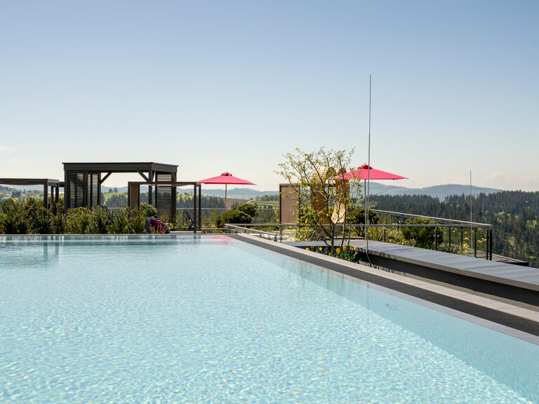 Pool auf sonniger Dachterrasse mit Sonnenschirmen und Waldpanorama vom Hotel Hüttenhof