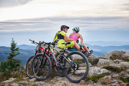 Radfahrer auf Berg im Bayerischen Wald mit Panorama im Sommer Zwei Radfahrer sitzen auf Felsen auf Berg im Bayerischen Wald