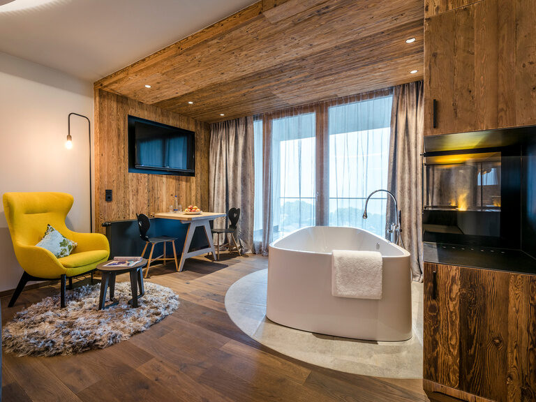 Modernes Hotelzimmer mit offener Badewanne und Balkon im Wellnesshotel Hüttenhof Modernes Hotelzimmer mit offener Badewanne, Sessel mit Beistelltisch und Balkon