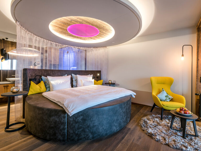 Modernes rundes Bett von Luxuszimmer im 4-Sterne-Hotel Hüttenhof Modernes rundes Bett, daneben sessel mit beistelltisch, darüber große Wandleuchte
