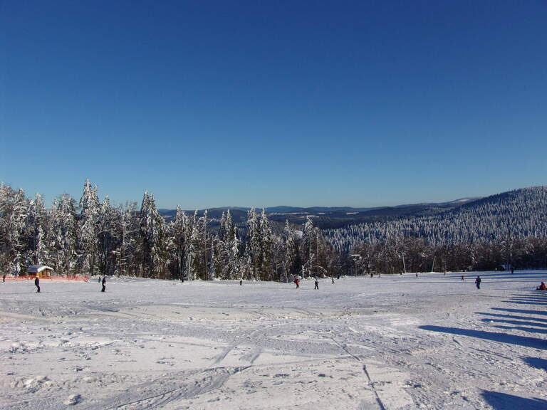 Skipiste umgeben von schneebedeckter Winterlandschaft im Bayerischen Wald Schneebedeckte Piste mit Skifahrern umgeben von Wäldern nahe dem Luxushotel Hüttenhof