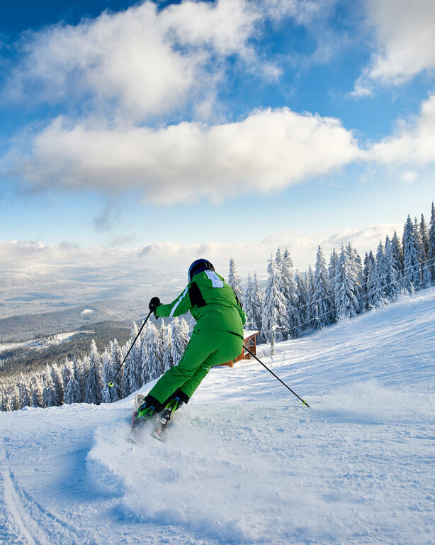 Skifahrer im grünen Skianzug bei Abfahrt auf schneebedeckter Piste