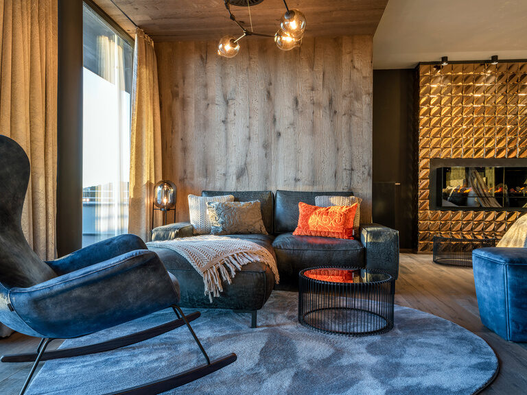 Sofa, Sessel und Kamin in moderner Luxussuite im Luxushotel Hüttenhof Sofa mit kleinem Tisch, Sessel und glänzendem Kachel-Kamin in moderner Luxussuite