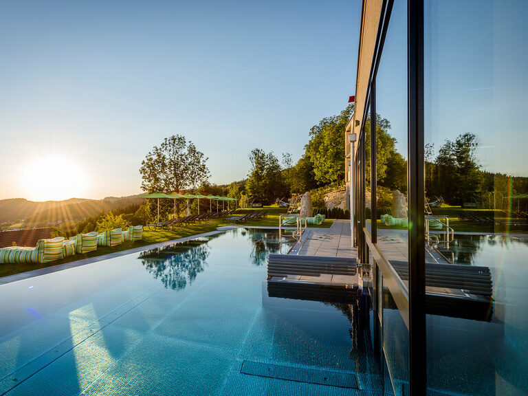 Die ersten Sonnenstrahlen des Tages legen sich über den Pool und das Hotel Hüttenhof im Bayerischen Wald.