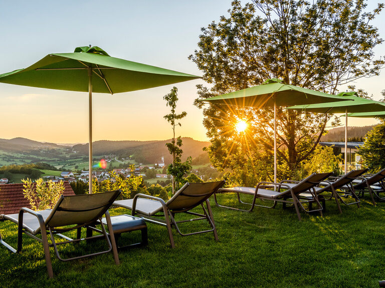 Sonnenschirme und Liegen im sonnenbeschienenen Garten, mit Blick auf den Bayerischen Wald