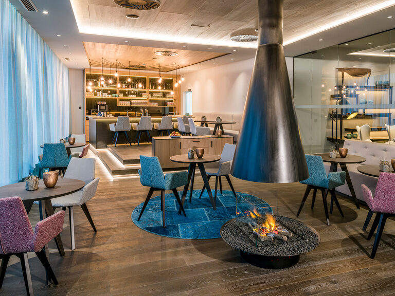 Spa-Bistro mit offenem Kamin im 4-Sterne-Luxushotel Hüttenhof Farbenfrohes Spa-Bistro mit offenem Kamin und runden Tischen im 4-Sterne-Wellnesshotel Hüttenhof