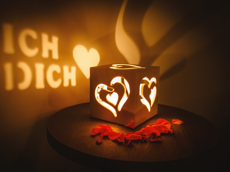 Teelicht in Herz-Holzbox, Rosenblätter und 'Ich liebe dich'-Lichtschrift an der Wand