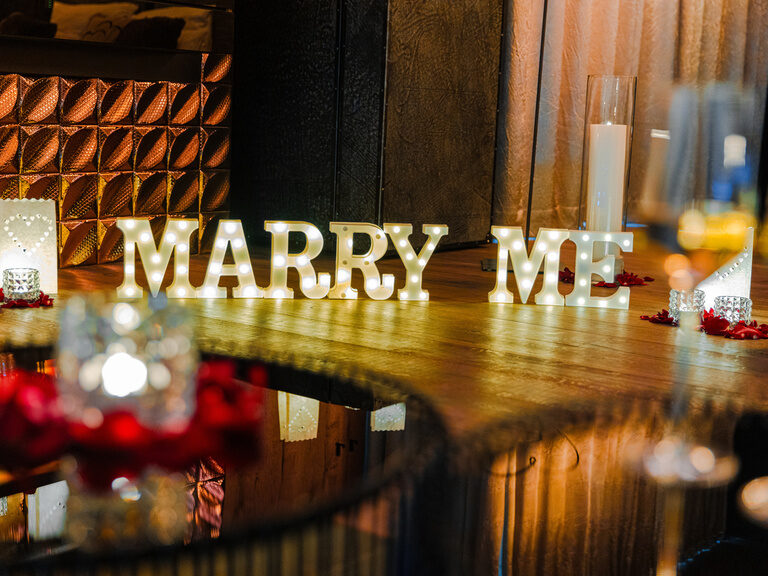 Teelicht in Herz-Holzbox, Rosenblätter und 'Ich liebe dich'-Lichtschrift an der Wand