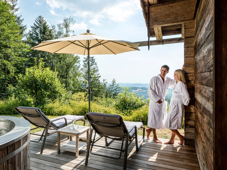 Pärchen auf Terrasse des Chalets mit Whirlpool und Ausblick auf den bayerischen Wald