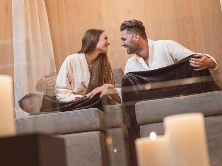 Turtelndes Liebespaar im Bademantel sitzt auf einer Liege im 4 Sterne Luxushotel Hüttenhof im Bayerischen Wald