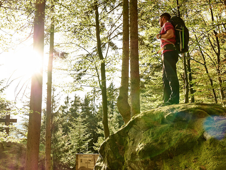 Wanderer steht auf einem Felsen und blickt auf die Sonne im Bayerischen Wald