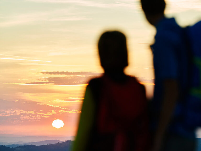 Menschen, von hinten gesehen, bewundern einen malerischen Sonnenuntergang im Bayerischen Wald