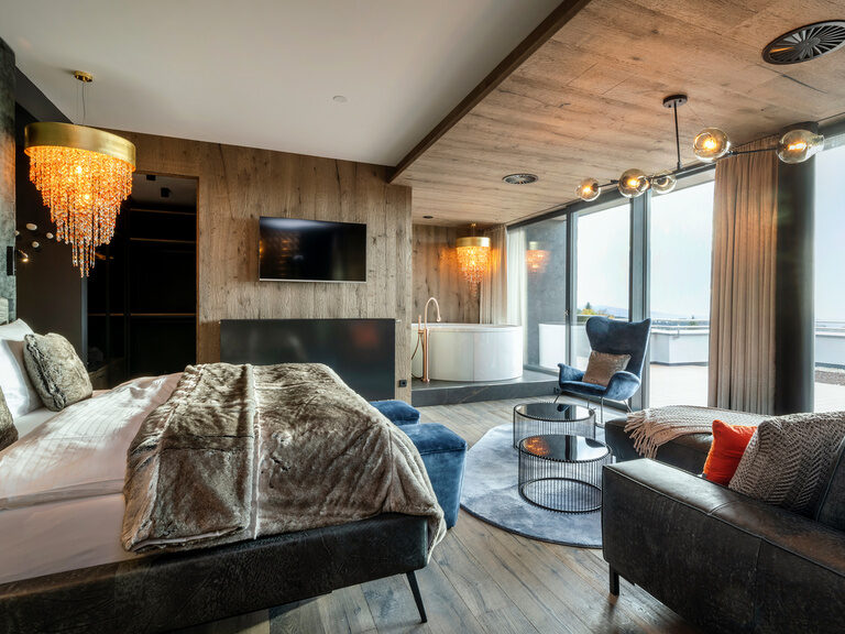 Modernes Luxuszimmer mit Balkon und Badewanne im Hotel Hüttenhof Luxuszimmer mit Bett, Kronleuchter großer Badewanne und Wohnbereich, Balkon