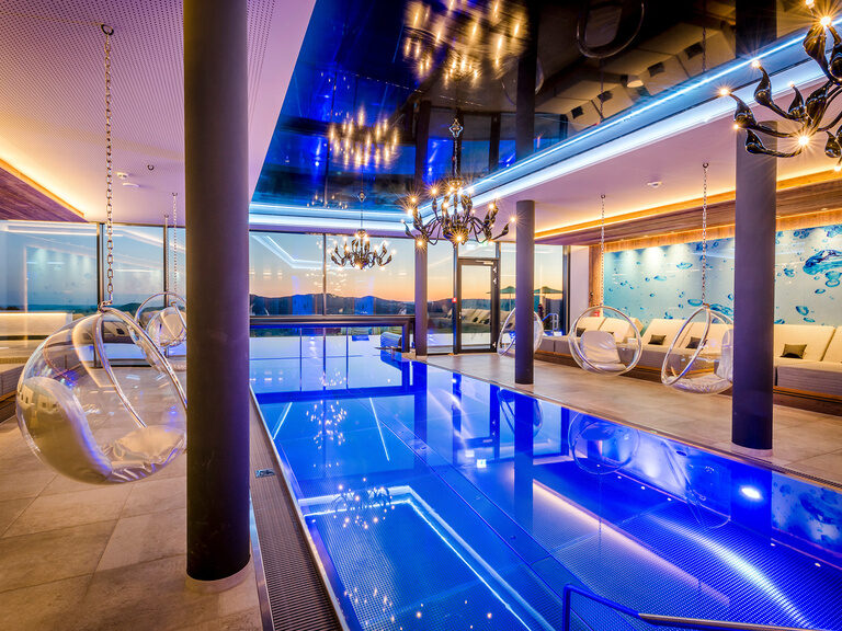 Beleuchteter, blauer Innenpool in der Dämmerung im Luxushotel Hüttenhof Beleuchteter, blauer Innenpool in der Dämmerung mit Panoramablick auf Bayerischen Wald